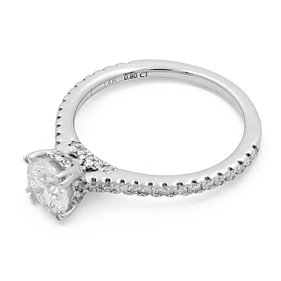 A stunning 14K White Gold Women's Contemporary Engagement Ring with 0.20Tw Round Diamonds featuring a prominent round diamond in the center, placed in a four-prong setting, and a band encrusted with smaller round diamonds. Crafted from 14K white gold, the inside of the band is marked with "Miral Jewelry".