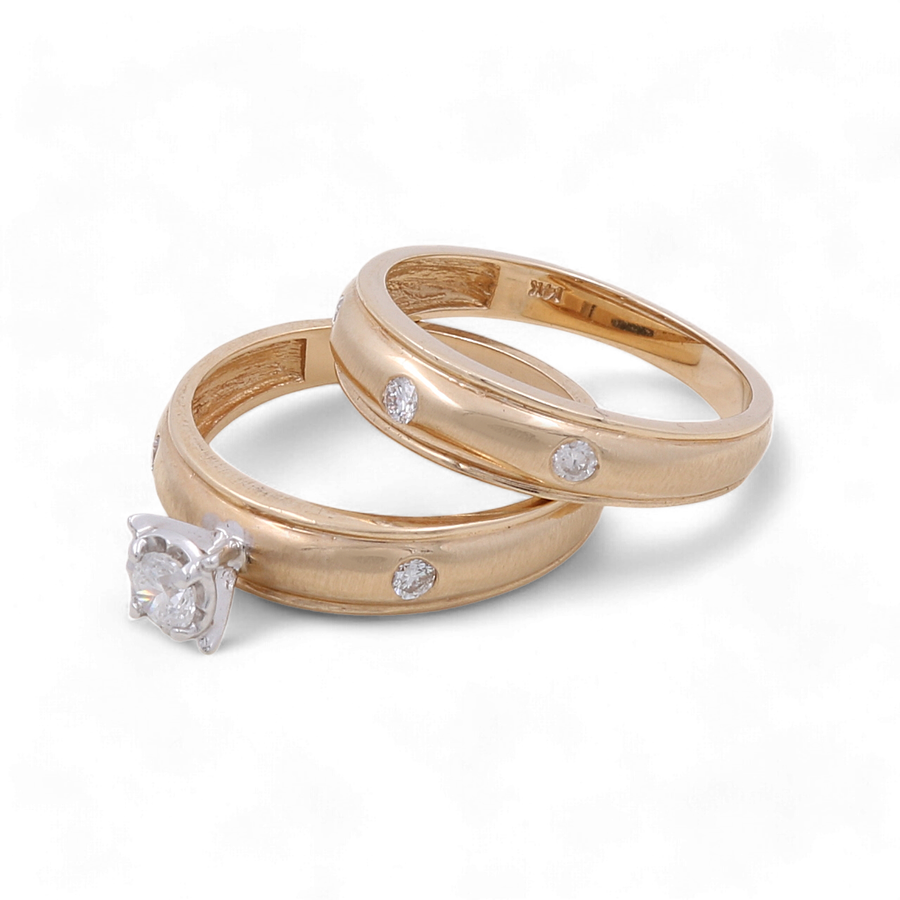 Miral Jewelry's 14K Yellow Gold Bridal Woman Rings with Diamonds: one adorned with a central diamond and the other featuring small embedded diamonds, delicately overlap on a white background—a perfect choice for the elegant bride seeking sophistication.