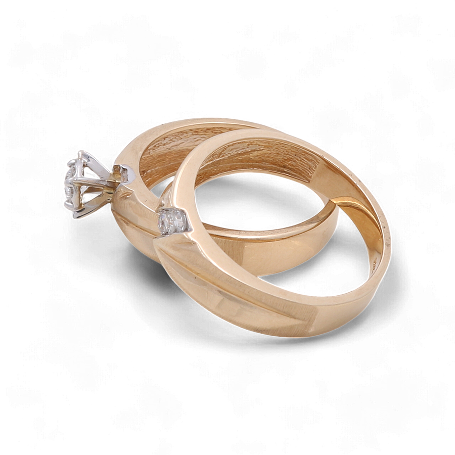 Two gold rings, from the Miral Jewelry collection, lie intertwined on a white background. One ring is a 14K Yellow Gold Bridal Woman Ring with Diamonds featuring an exquisite diamond setting, while the other showcases a solitary diamond embedded in the band, highlighting its elegant design.