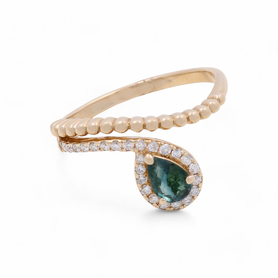 The 14K Yellow Gold Woman Fashion Ring by Miral Jewelry features a teardrop-shaped green gemstone surrounded by small diamonds. The ring is crafted in 14K yellow gold and boasts a unique design with a beaded band on one side and a smooth band on the other.