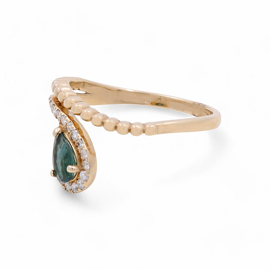 Introducing the 14K Yellow Gold Woman Fashion Ring by Miral Jewelry, a stunning piece featuring a pear-shaped green gemstone surrounded by delicate diamonds on one side and crafted with intricate beaded detailing on the band.