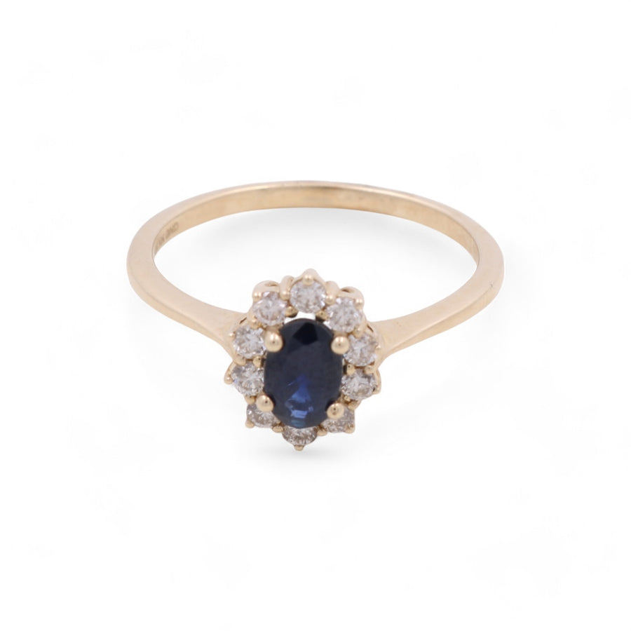 The 14K Yellow Gold Woman Ring with Diamonds and Sapphire by Miral Jewelry features an oval-shaped blue sapphire at its center, surrounded by small clear diamonds arranged in a flower-like design on a white background. This piece of jewelry exudes elegance and timeless beauty.