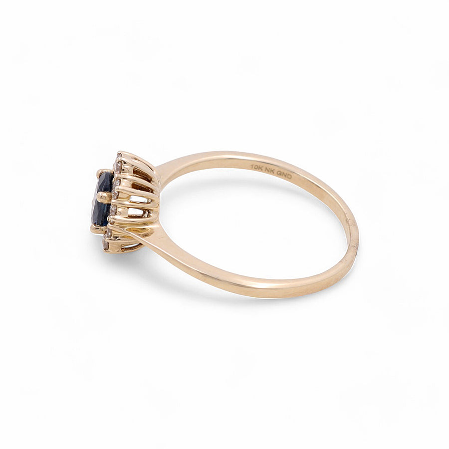 The 14K Yellow Gold Woman Ring with Diamonds and Sapphire by Miral Jewelry features a striking blue gemstone set in a six-prong setting, captured beautifully in a side view on a white background. This exquisite piece of jewelry embodies timeless elegance and sophistication.