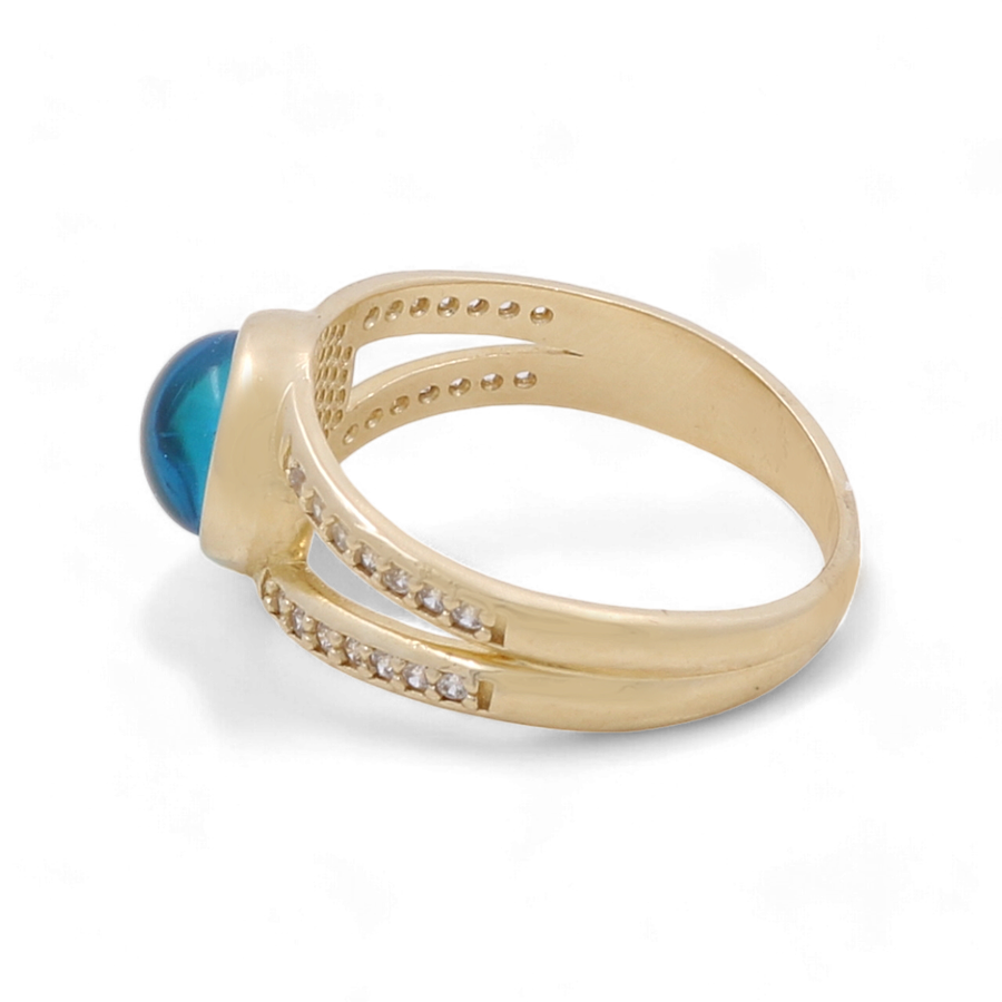 Introducing the 14K Yellow Gold Fashion Evil Eye with Zirconias Women's Ring by Miral Jewelry. This exquisite piece showcases a striking blue gemstone surrounded by two rows of delicate white zirconias set on the band, making it an ideal choice for those who appreciate elegance with a touch of timeless charm.