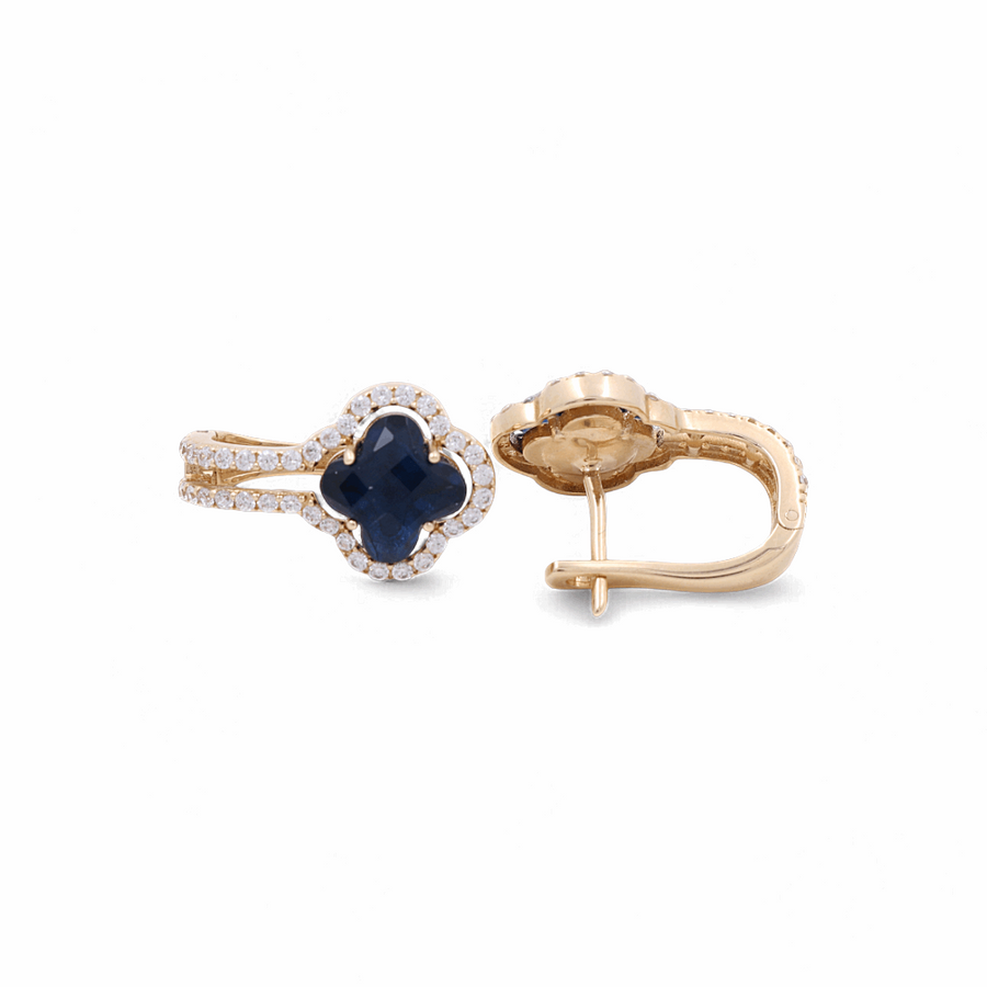 A pair of Miral Jewelry's 14K Yellow Gold Blue Stone Huggie Women's Earrings with Cz, featuring a four-leaf clover shape with a dark blue center stone surrounded by small clear stones, displayed against a white background—perfect for women's fashion.