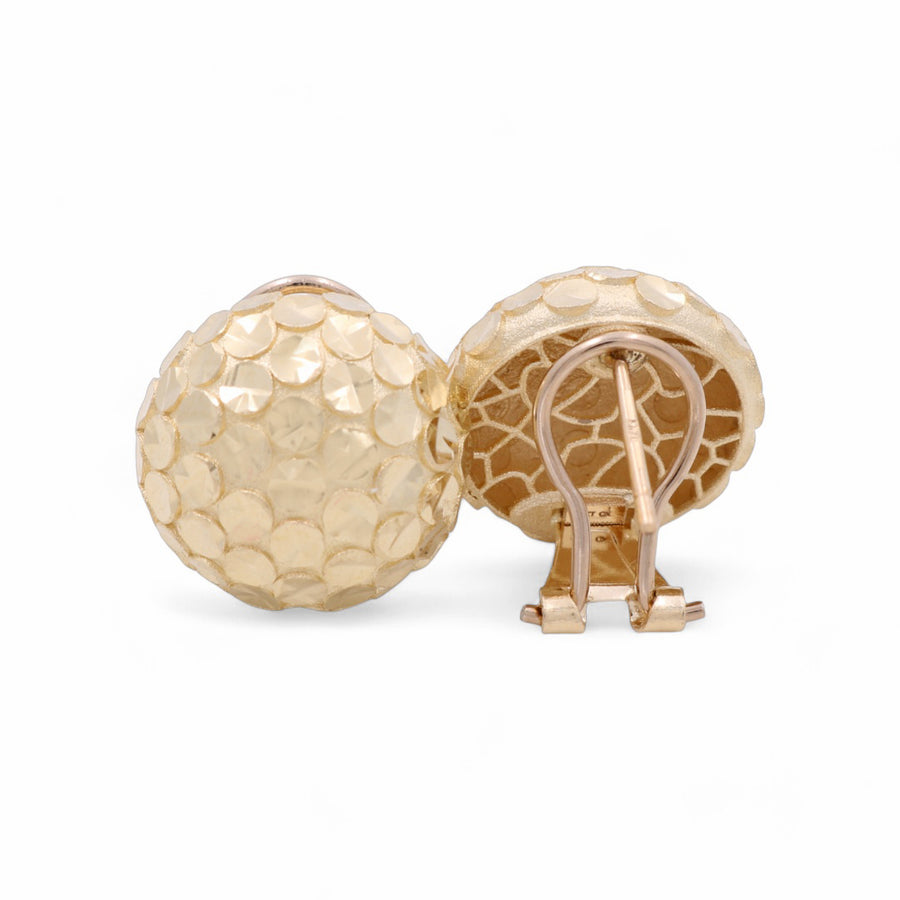 A pair of 14K yellow gold button women's earrings from Miral Jewelry, featuring a textured, dimpled surface and clip-on backs that reveal the clip mechanism.