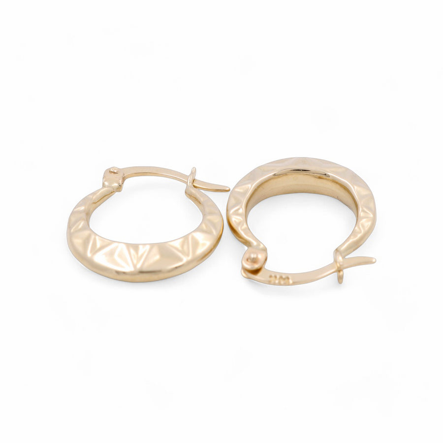 A pair of 14K Yellow Gold Hoop Women's Earrings by Miral Jewelry with a diamond pattern is displayed against a white background. One earring lies down, while the other stands upright, making them perfect as elegant women's earrings.