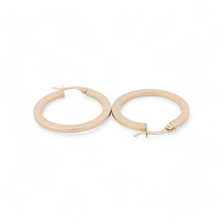 A pair of 14K yellow gold hoop earrings by Miral Jewelry with textured surfaces, laid flat on a white background, showcasing their classic design.