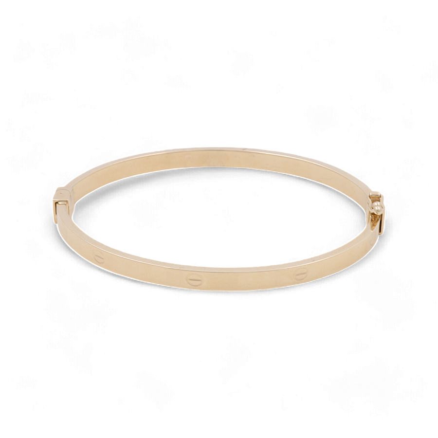 The 14K Yellow Gold Women's Fashion Bangle Bracelet by Miral Jewelry features a hinged design and a series of small engraved screw motifs, perfect for women's fashion.