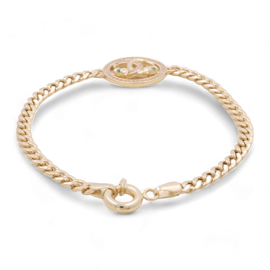 A 14K Gold Fashion Bracelet by Miral Jewelry, showcasing a central circular emblem adorned with detailed designs and small green color stones, along with cubic zirconias.