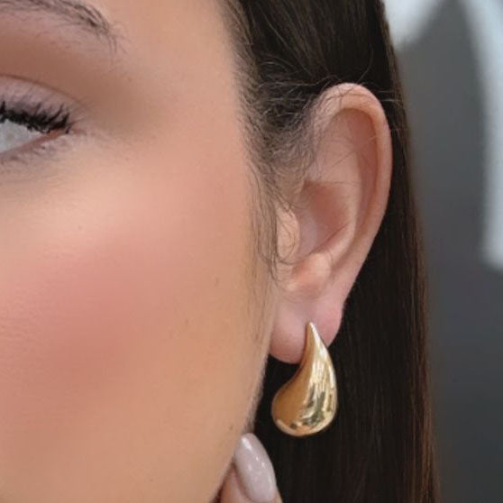 Close-up of a woman wearing luxurious Miral Jewelry 14K Yellow Gold Extra Large Drop Earrings, with her fingers touching her cheek.