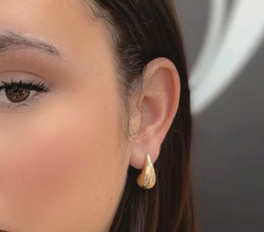 Close-up of a woman's ear adorned with Miral Jewelry's elegant 14K Yellow Gold Medium Drop Earrings, featuring intricate designs. Only part of her face is visible.