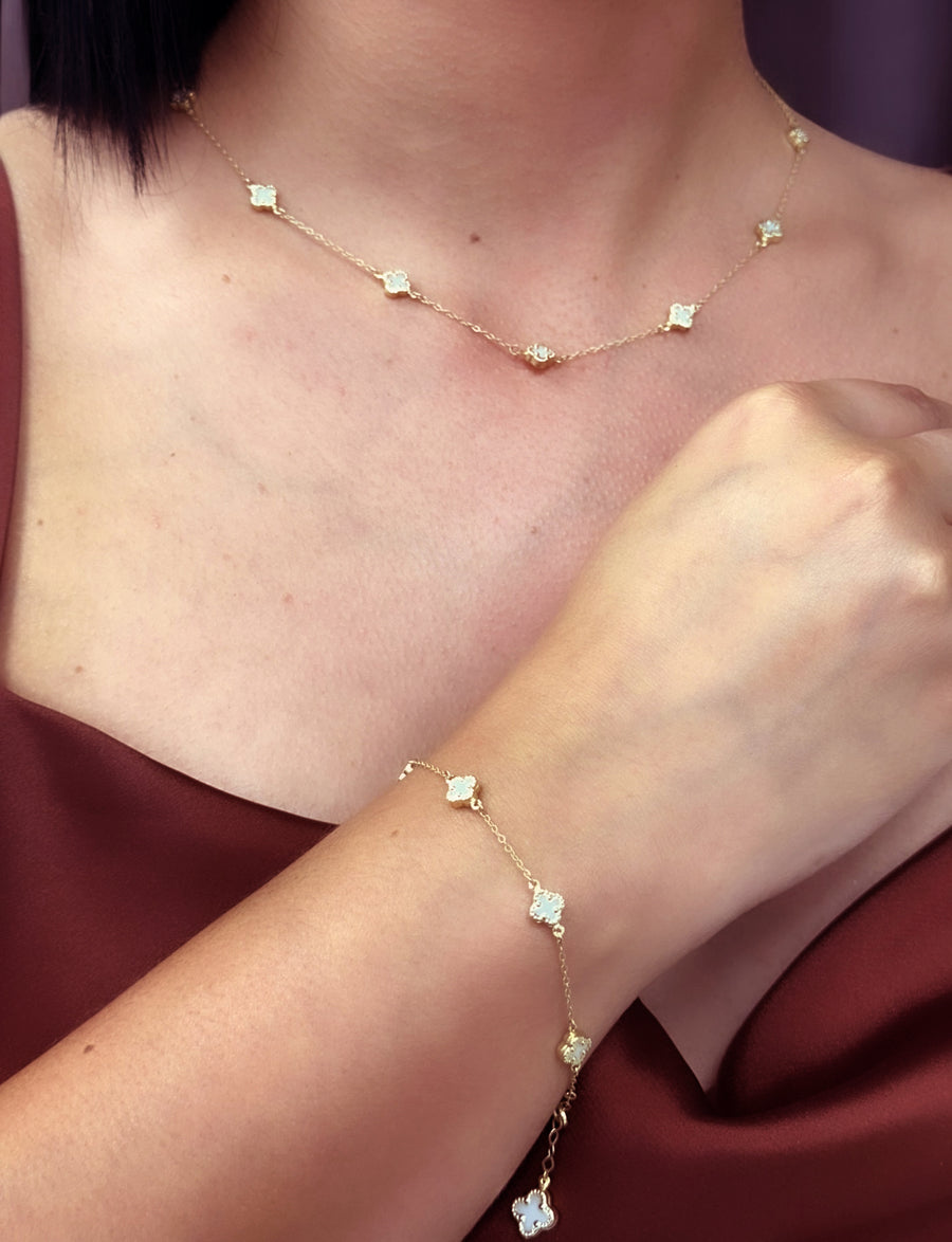 Close-up of a person wearing the Miral Jewelry 14K Yellow Gold Fashion Clover with Mother of Pearl Set, which includes a delicate necklace and bracelet, each adorned with small mother of pearl floral-shaped charms. They are dressed in a sleeveless maroon top.