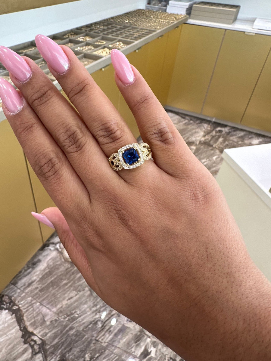 A hand with pink manicured nails displaying an anillo 14k piedra azul by Miral Jewelry is shown in a jewelry store.