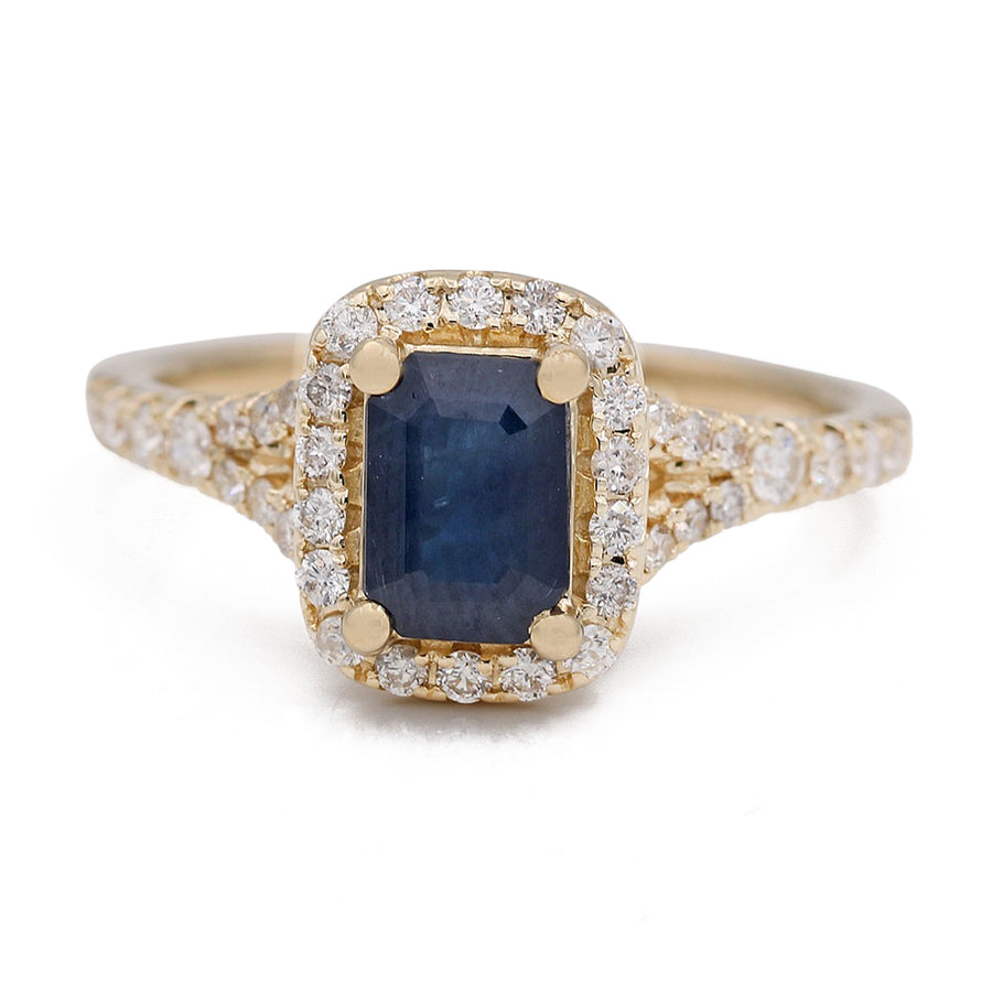 A stunning 14 karat yellow gold cocktail fashion ring featuring a rectangular blue gemstone surrounded by small diamonds and adorned with additional diamonds along the band. Introducing the Yellow Gold Sapphire and Diamonds Ring by Miral Jewelry.