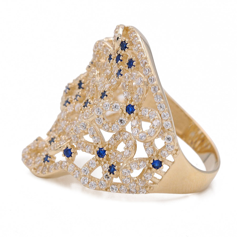 This Yellow Gold 14k Fashion Ring With Blue and White Cz by Miral Jewelry boasts an intricate, lace-like design adorned with small blue gemstones and numerous small white cubic zirconia stones, making it a truly luxurious piece.